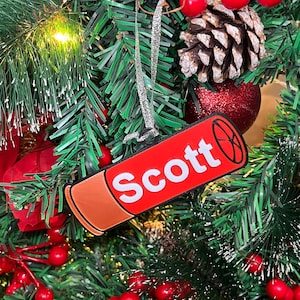 May include: Red and orange shotgun shell Christmas ornament with the name "Scott" written in white letters.