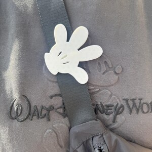 Puede incluir: Una ri&ntilde;onera negra y gris con cierre de cremallera. La ri&ntilde;onera se lleva sobre una sudadera gris con el texto "Walt Disney World" bordado en la parte delantera. Una mano de Mickey Mouse de pl&aacute;stico blanco est&aacute; unida a la correa de la ri&ntilde;onera.