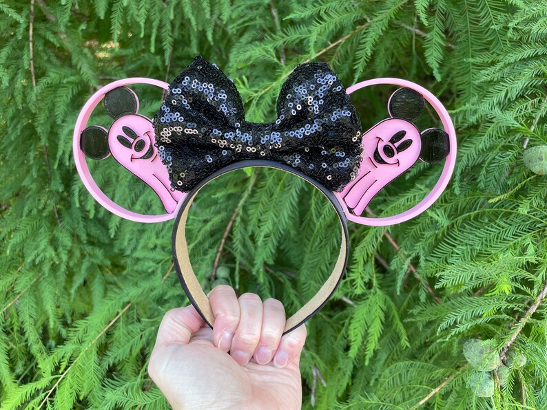 May include: Pink Mickey Mouse ears headband with a black sequined bow. The ears are shaped like ghosts with Mickey Mouse faces.