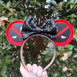 May include: Red and black mouse ears with a black sequin bow. The ears feature a Deadpool logo.