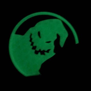 Pode incluir: Um adesivo verde que brilha no escuro com a silhueta de um personagem com um sorriso travesso. O personagem &eacute; do filme popular "O Estranho Mundo de Jack".