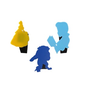 May include: Three silhouette figures of Disney characters: Belle in a yellow dress, the Beast in blue, and Prince Adam in blue, reading a book. The figures are made of plastic and are attached to a black base.