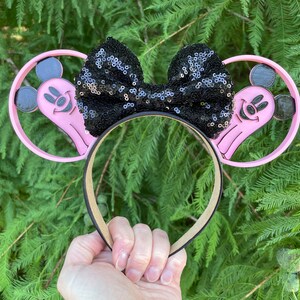 May include: Pink Mickey Mouse ears with a black sequin bow. The ears feature a ghost Mickey Mouse design.
