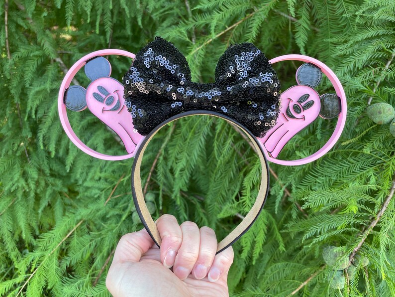 May include: Pink Mickey Mouse ears with a black sequin bow. The ears feature a ghost Mickey Mouse design.