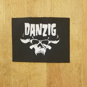 May include: Black and white embroidered patch featuring the word "DANZIG" and a skull with horns.