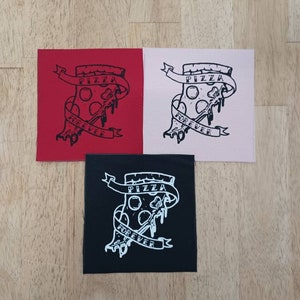 May include: Three square patches with a pizza slice design and the words "Pizza Forever" in a banner. The patches are red, pink, and black, with a white graphic. The patches are on a wooden surface.