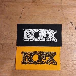 May include: Two rectangular patches with the word "NOFX" in a bold, stylized font. One patch is black with white lettering, and the other is yellow with black lettering. The patches are likely for clothing or accessories.
