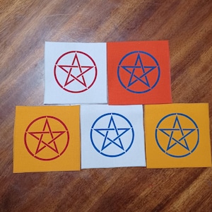 May include: Five square patches in white, orange, yellow, and blue. Each patch features a pentagram design in a contrasting color, enclosed within a circle. The patches are arranged on a wooden surface.
