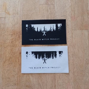 May include: Two black and white iron-on patches with a stylized forest scene and the text "The Blair Witch Project".