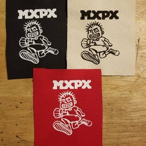 May include: Three fabric patches with the text "MXPX" above a white cartoon figure. One patch is black, one is off-white, and the third is red. The cartoon figure is running with a determined expression.