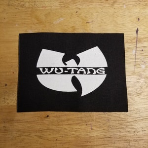 May include: Black rectangular patch with the white Wu-Tang Clan logo. The logo features a stylized W shape with the words "WU-TANG" in white block letters across the center.