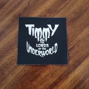 Puede incluir: Parche de tela negro con texto blanco que dice "Timmy & The Lords of the Underworld".