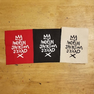 May include: Three fabric patches with the same design. The design features a crown, the words "Andrew Jackson Jihad", and an X. The patches are red, black, and white.