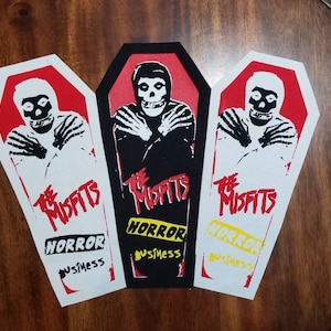 May include: Three coffin-shaped patches featuring The Misfits logo and a skull graphic. The patches have a red, black, and white color scheme with the words "HORROR BUSINESS" in yellow and white.
