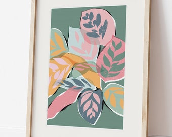 May include: A framed art print featuring a botanical illustration of colorful leaves. The leaves are in shades of pink, orange, and blue against a green background. The artwork is displayed in a light wood frame, leaning against a white wall.