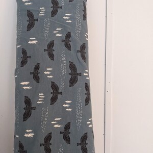 May include: A blue fabric with a repeating pattern of black birds flying and white stylized trees. The fabric is folded and rolled up.