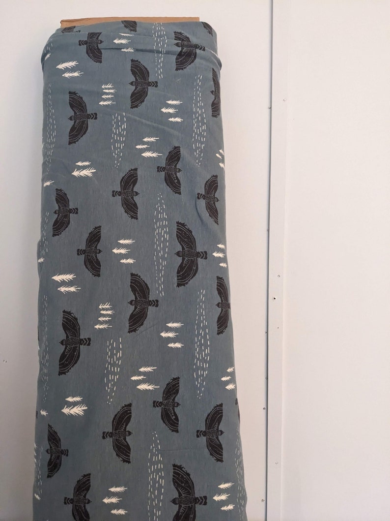 May include: A blue fabric with a repeating pattern of black birds flying and white stylized trees. The fabric is folded and rolled up.