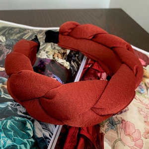 May include: A wide, braided headband made of a soft, rust-colored fabric. The headband is thick and has a slightly textured surface.