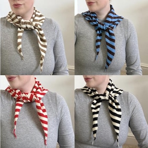 May include: Four striped scarves in different color combinations: brown and white, blue and brown, red and white, and black and white. Each scarf is tied around the neck, showcasing the striped pattern and the scarf's design.