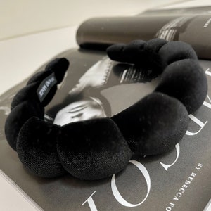 Peut inclure: Un serre-tête en velours noir avec un design rond et bouffant. Le serre-tête porte l'inscription "HAND MADE" sur le côté.