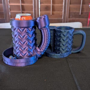 May include: A 3D printed purple and blue can holder with a built-in dice tower and a matching mug. The can holder has a textured design and a small tray for dice. The mug has a handle and a textured design.