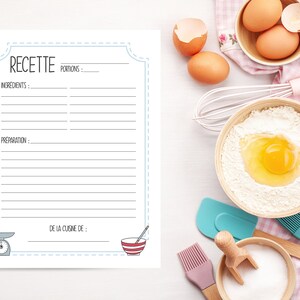 May include: A white recipe sheet with the word "RECETTE" at the top, along with spaces for ingredients and preparation instructions. A scale and a bowl are illustrated at the bottom. Baking ingredients and tools surround the sheet.