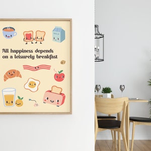 May include: A framed print with a yellow background and the text "All happiness depends on a leisurely breakfast."  The print features cartoon illustrations of breakfast foods, including a cup of coffee, toast, bacon, an egg, a croissant, an apple, a glass of orange juice, and a toaster.