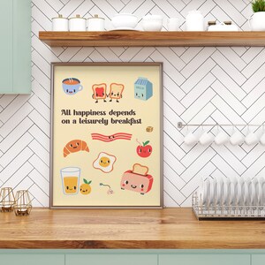 May include: A framed print with a yellow background and a quote that reads "All happiness depends on a leisurely breakfast." The print features various breakfast foods with cute faces, including toast, bacon, eggs, a croissant, a glass of orange juice, a cup of coffee, and a carton of milk.