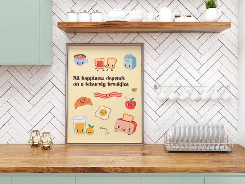May include: A framed print with a yellow background and a quote that reads "All happiness depends on a leisurely breakfast." The print features various breakfast foods with cute faces, including toast, bacon, eggs, a croissant, a glass of orange juice, a cup of coffee, and a carton of milk.