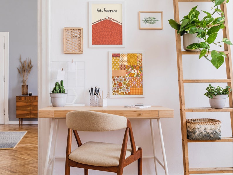 May include: A home office desk with a white chair, a wooden ladder shelf with plants, and artwork on the wall. The artwork includes a print with the text "Knit Happens" and a colorful patterned print.