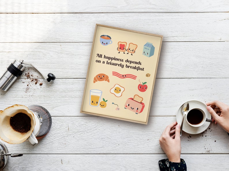 May include: A beige framed print with a yellow background and colorful cartoon illustrations of breakfast foods. The text reads "All happiness depends on a leisurely breakfast."