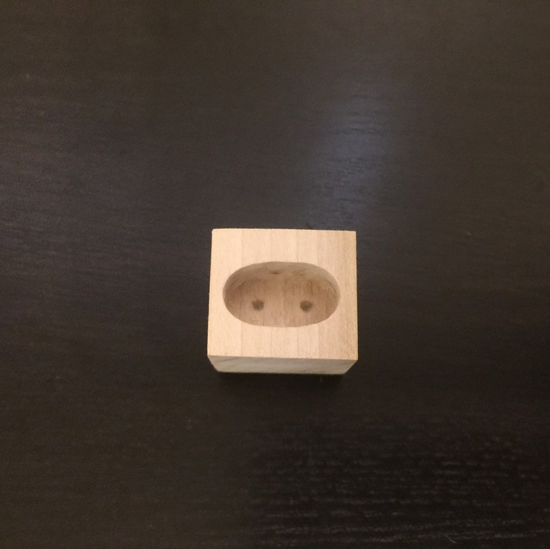 May include: A small wooden block with a cutout oval shape in the center. The oval has two small holes drilled into it.