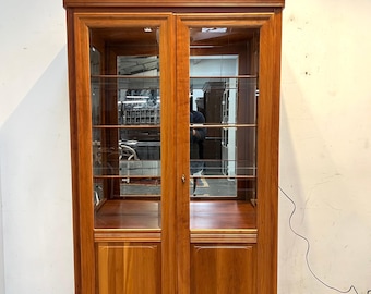 Vitrina de madera de cerezo con puertas de cristal e iluminación.