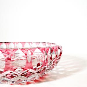 Pode incluir: Uma tigela de vidro lapidado transparente com um interior rosa vibrante. A tigela apresenta um padrão geométrico de diamantes e ovais, criando uma superfície texturizada. A borda também é rosa, aumentando o apelo decorativo. A tigela é provavelmente usada para servir ou exibir.