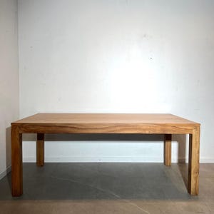 Puede incluir: Una mesa rectangular de madera con un acabado marrón claro. La mesa tiene un diseño sencillo con cuatro patas cuadradas y una superficie lisa. La mesa mide aproximadamente 183 cm de largo, 91 cm de ancho y 76 cm de alto.