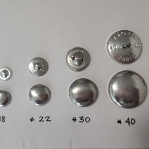 May include: Assortment of silver metal buttons in various sizes, labeled #18, #22, #30, and #40. The largest button has the text "BUFFET 40 PARIS 40" engraved on it.