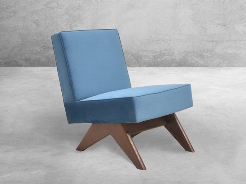 May include: A blue upholstered chair with a wooden frame and angled legs. The chair is sitting on a concrete floor.