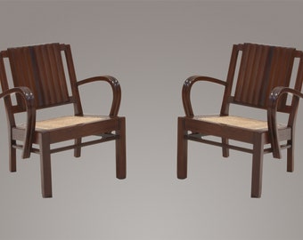 May include: Two dark brown wooden chairs with cane seats. The chairs have a slatted back and curved arms.