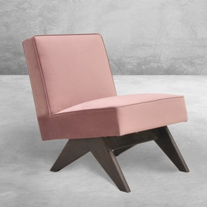 May include: A pink velvet armchair with a dark wood frame and angled legs. The chair is sitting on a concrete floor.