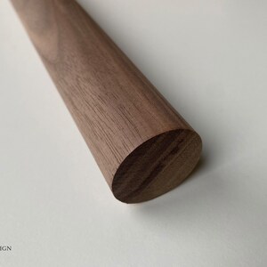Puede incluir: Primer plano de una varilla de madera redonda hecha de madera de nogal. La madera tiene un color marr&oacute;n intenso y un acabado liso y pulido.