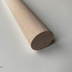 Puede incluir: Primer plano de una varilla de madera de color marr&oacute;n claro con un extremo redondeado. La varilla es lisa y tiene una veta de madera natural.