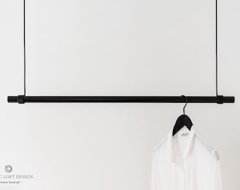 May include: A black metal clothing rod hangs from the ceiling with black cords. A white shirt hangs on a black hanger from the rod.