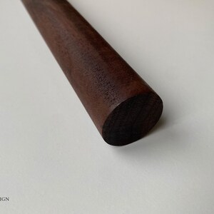 Puede incluir: Primer plano de un rodillo de madera marr&oacute;n oscuro. El rodillo es liso y tiene un extremo redondeado.