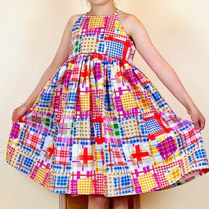 May include: A colorful patchwork dress with a halter neckline and a gathered skirt. The dress features a variety of colors and patterns, including red, blue, yellow, green, and pink.