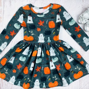 May include: A dark green long-sleeved dress with a pumpkin and ghost print. The dress has a gathered skirt and is perfect for Halloween.