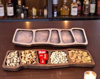May include: Two wooden serving trays, one empty and one filled with snacks including pistachios, cashews, chickpeas, and almonds. A small red box is in the center. A lit candle is nearby.