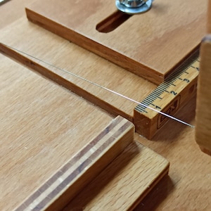 Pu&ograve; includere: Primo piano di uno strumento in legno con un righello e una vite in metallo. Lo strumento &egrave; utilizzato per tagliare la corda.