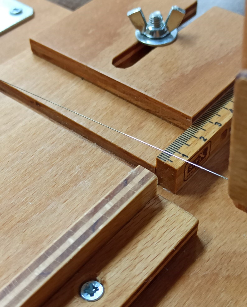 Pu&ograve; includere: Primo piano di uno strumento in legno con un righello e una vite in metallo. Lo strumento &egrave; utilizzato per tagliare la corda.