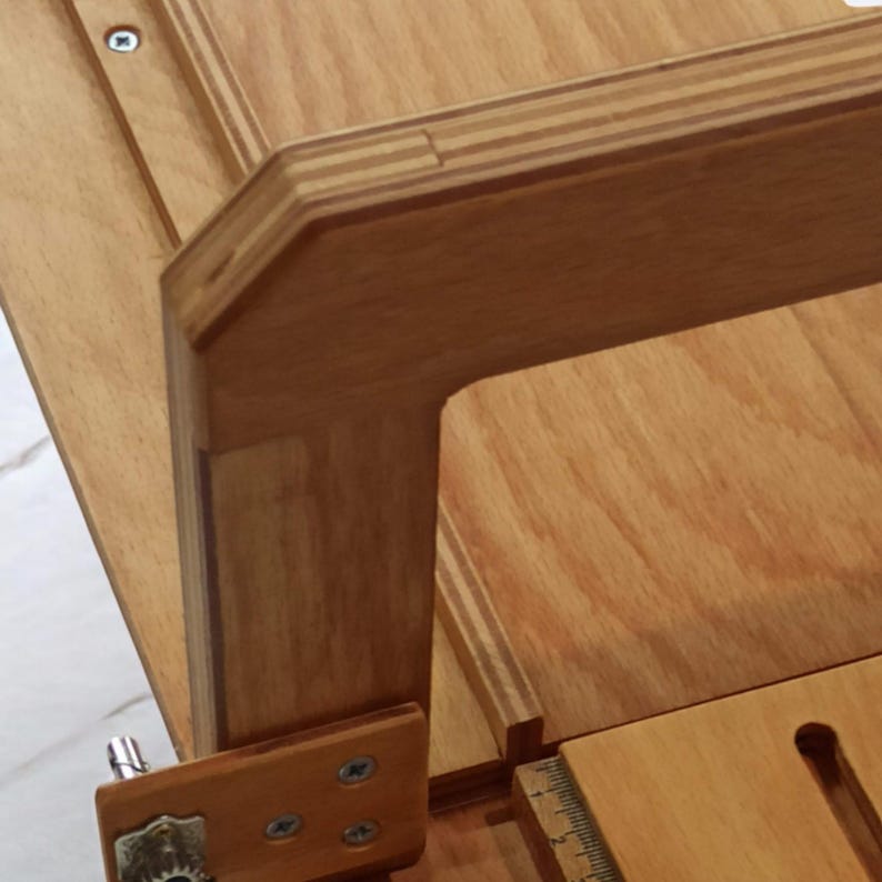 Pu&ograve; includere: Primo piano di un tavolo in legno con un piano in compensato e una cornice in legno. La cornice &egrave; realizzata con pi&ugrave; strati di legno, creando un motivo a strisce. Il tavolo ha un design semplice ed &egrave; realizzato in legno naturale.