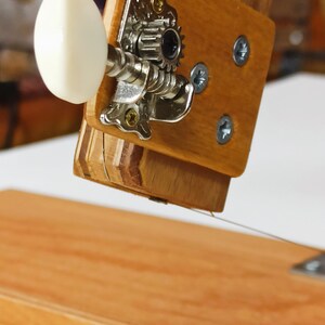 Pu&ograve; includere: Primo piano di un leggio in legno con un pirolo di accordatura argentato e una manopola bianca. Il leggio &egrave; fatto di pi&ugrave; strati di legno.